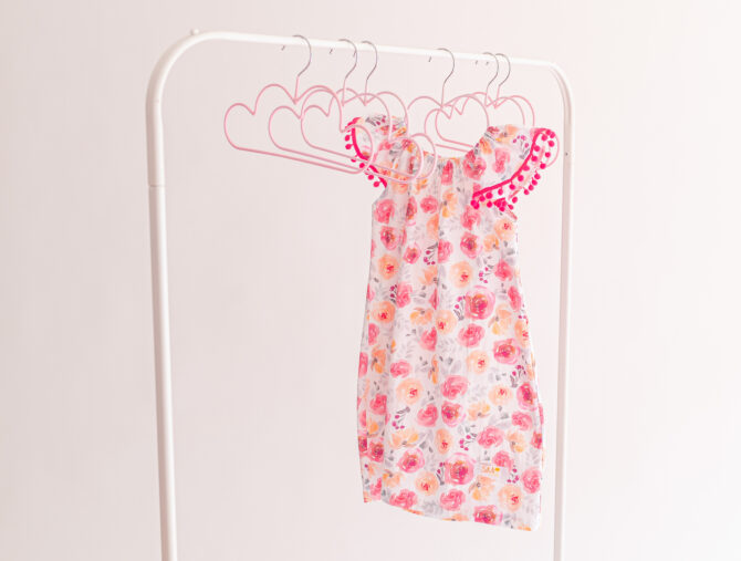 Dress with pink flowers and pompoms hanging on a rack